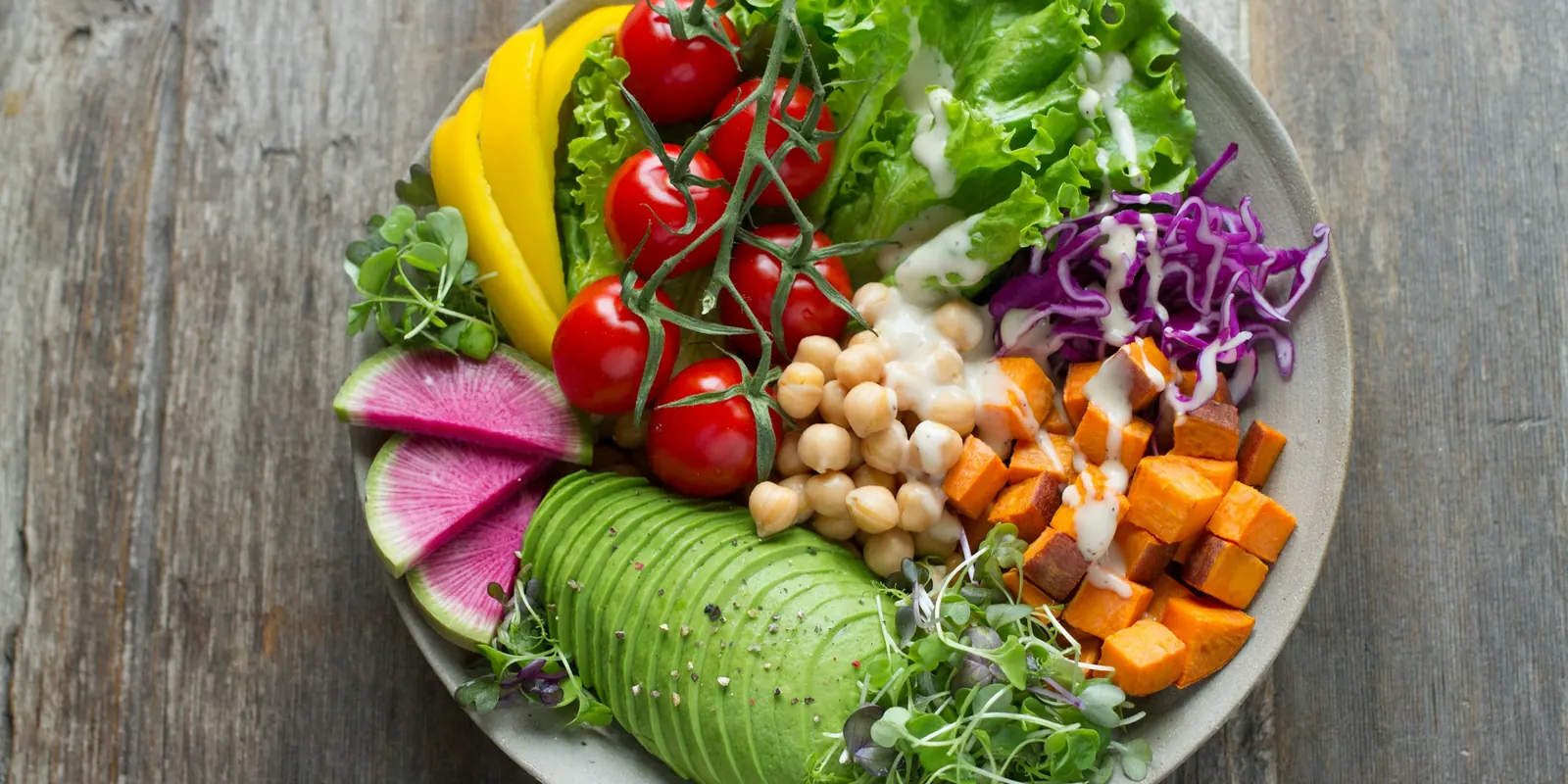 A colourful bowl of cherry tomatoes, chickpeas, avocado, roasted sweet potato, red cabbage and greens